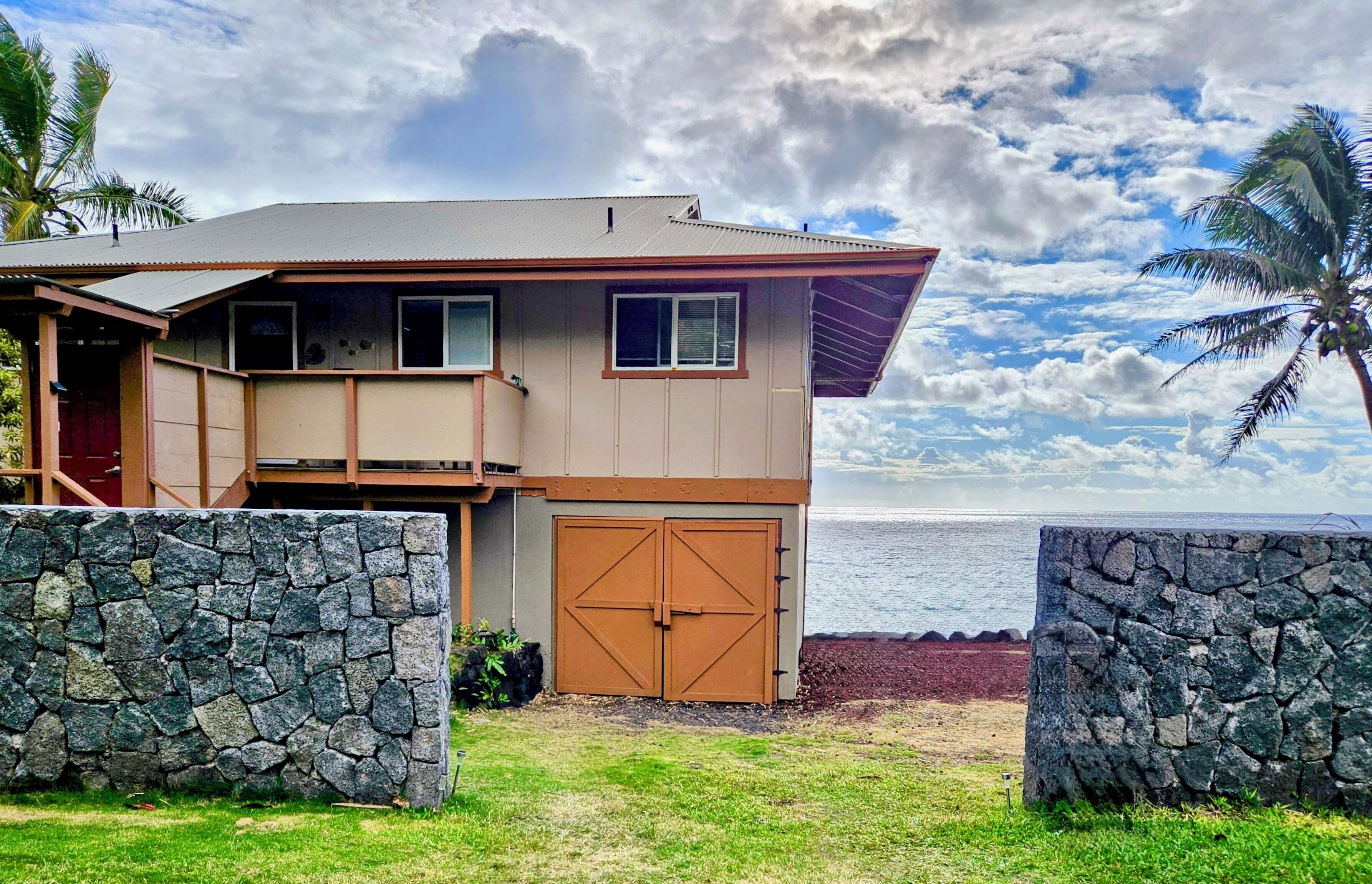 A two-story house with a stone wall in front, a garage, and a view of the ocean.