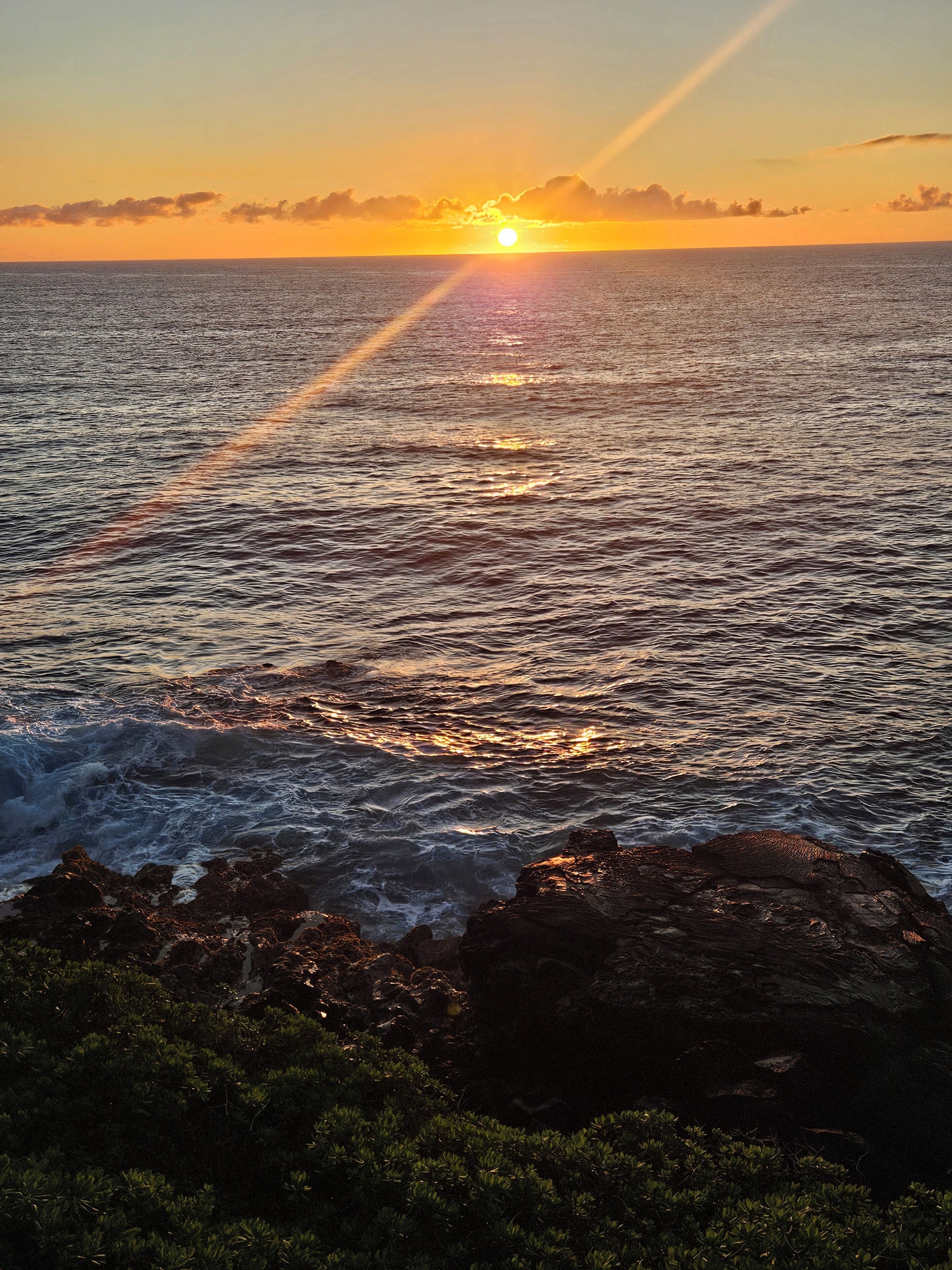 A sunset over the ocean with waves crashing onto rocks.