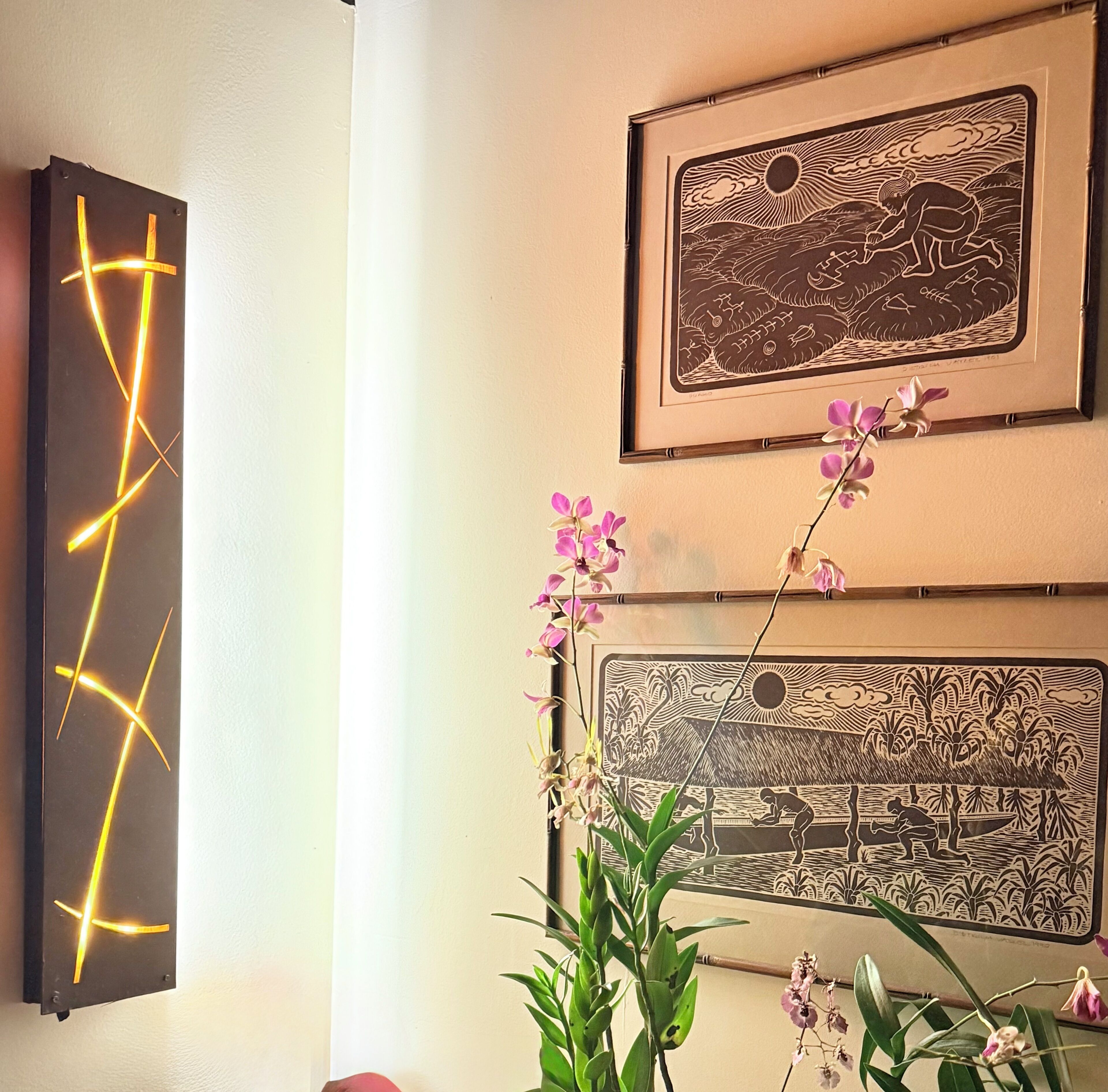 Een muur met twee ingelijste kunstwerken en een moderne lamp.