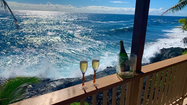 Un balcon avec vue sur l’océan, deux coupes de champagne et une bouteille dans un récipient en verre.