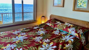 Une chambre avec un lit, une fenêtre donnant sur la mer et deux tableaux encadrés accrochés au mur.
