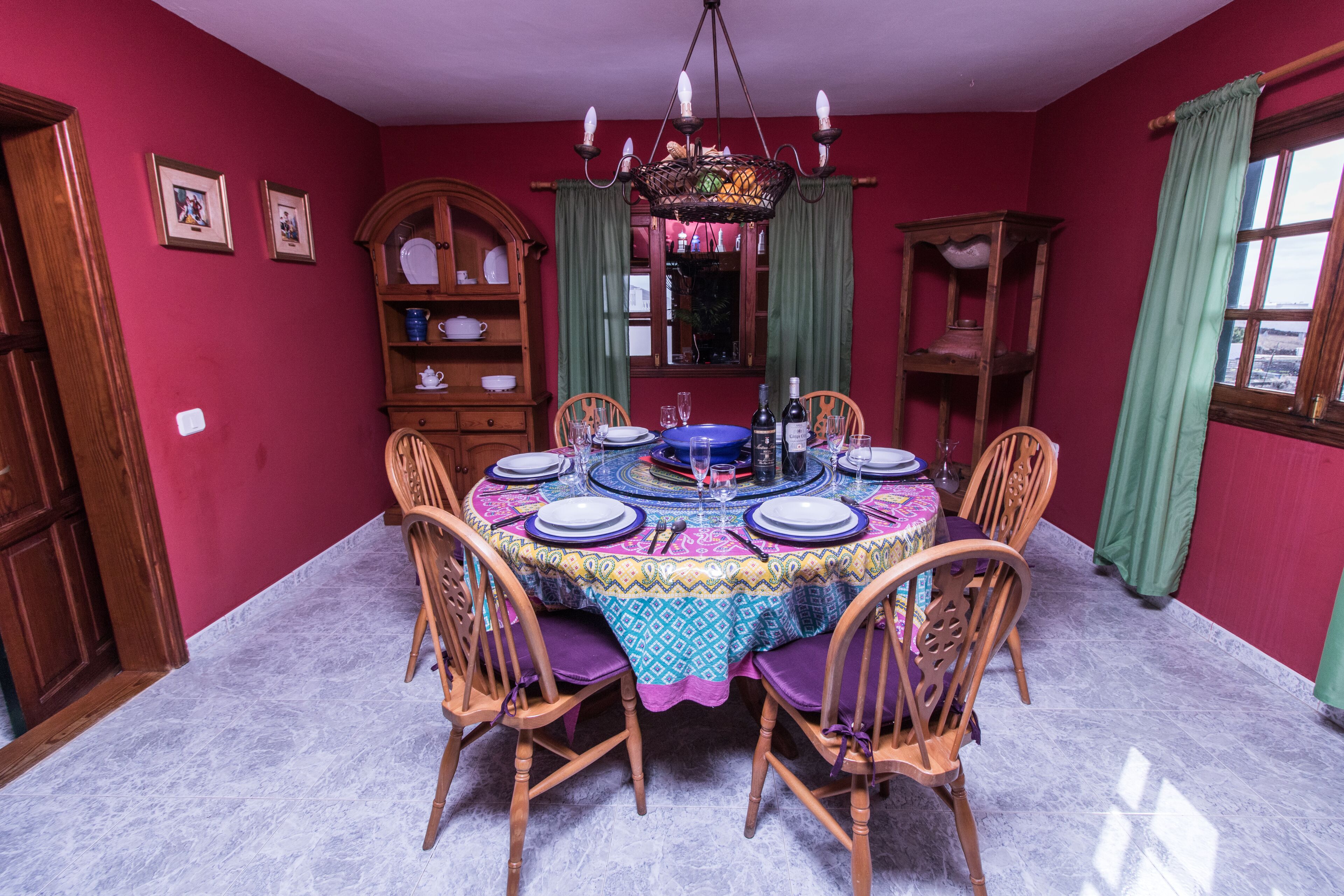 A dining room with a round table set for six, surrounded by wooden chairs.