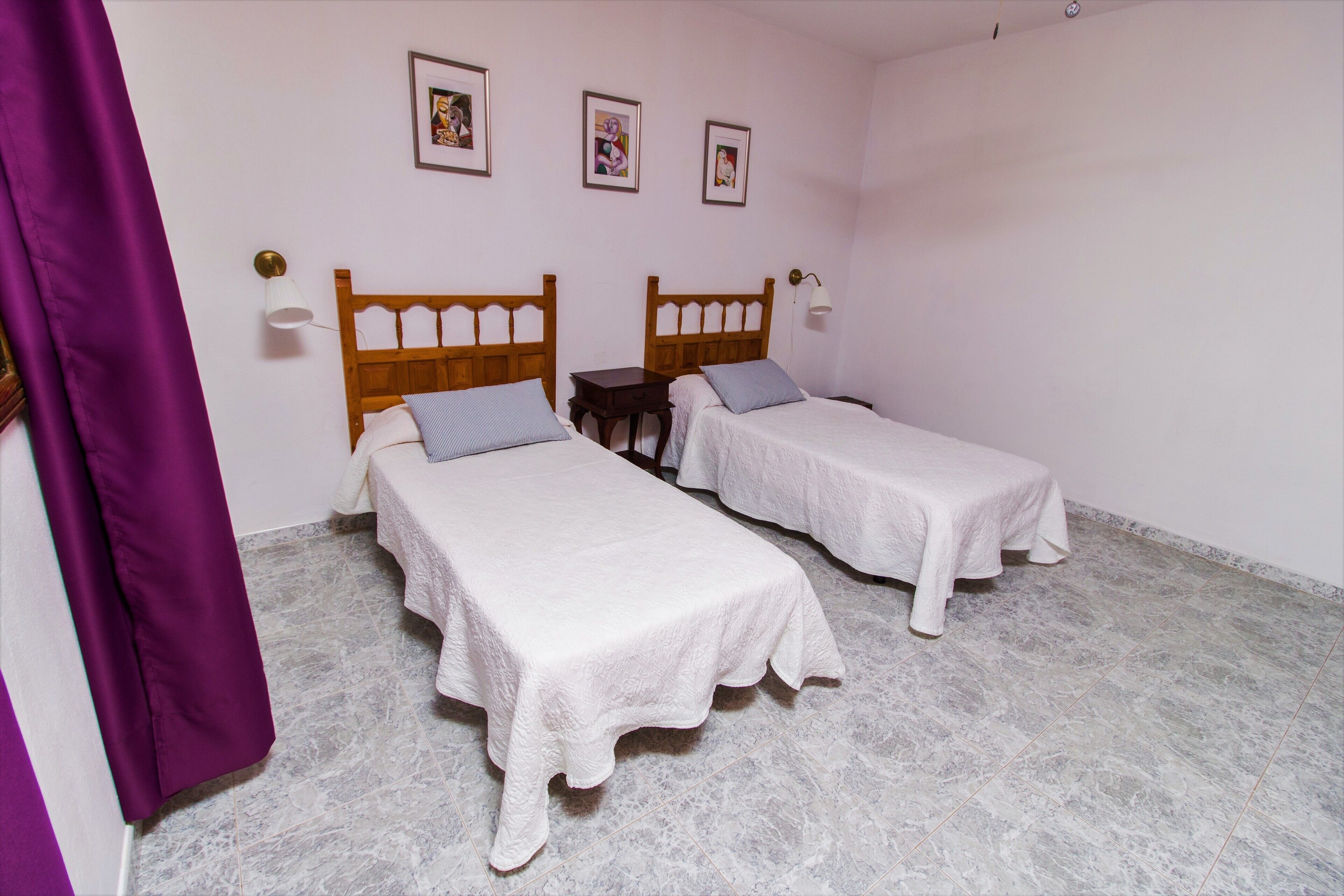 Una habitación con dos camas individuales, una mesita pequeña y una cortina morada.