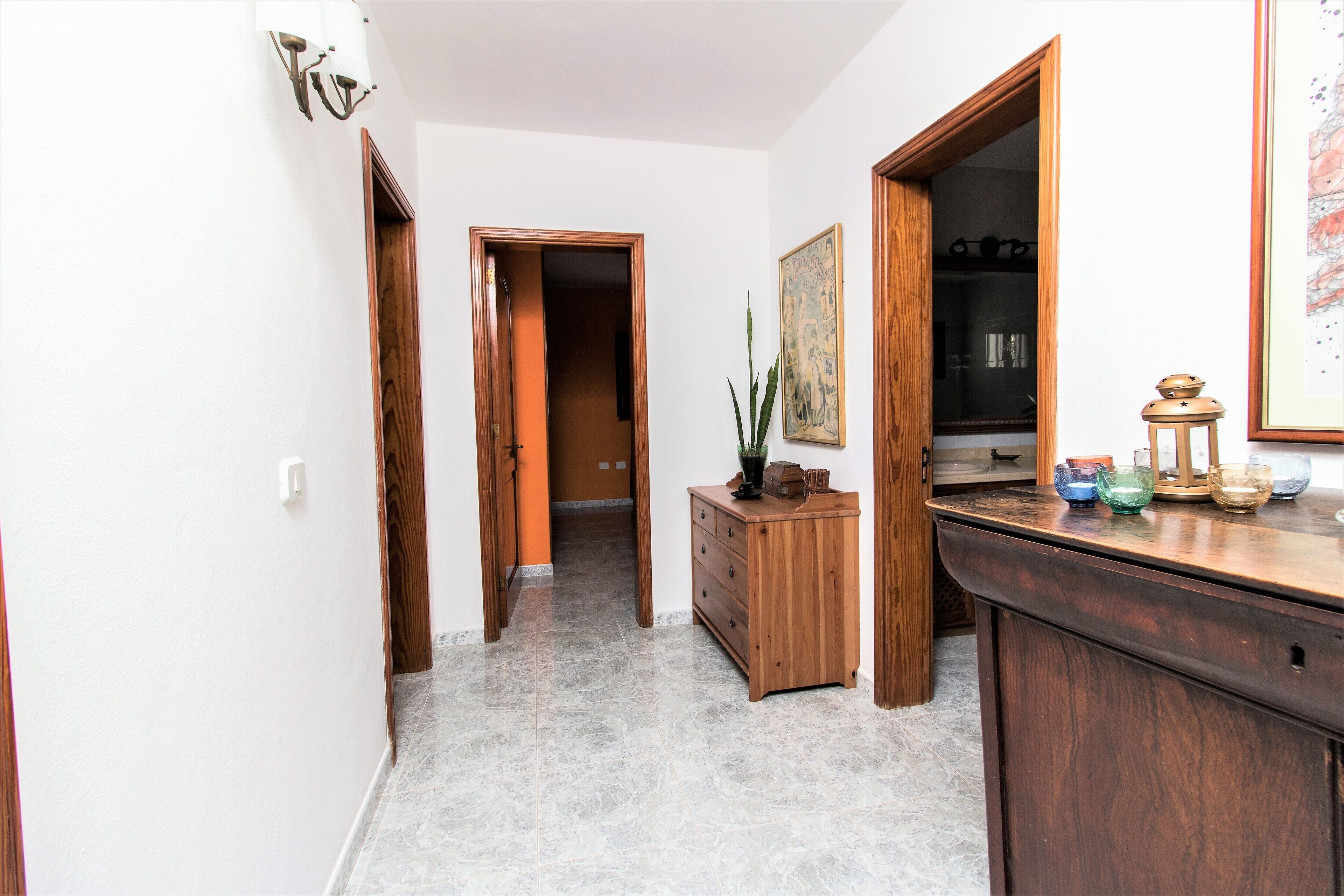 A hallway with wooden doors, a marble floor, a wooden dresser, and a small table with decorative items.