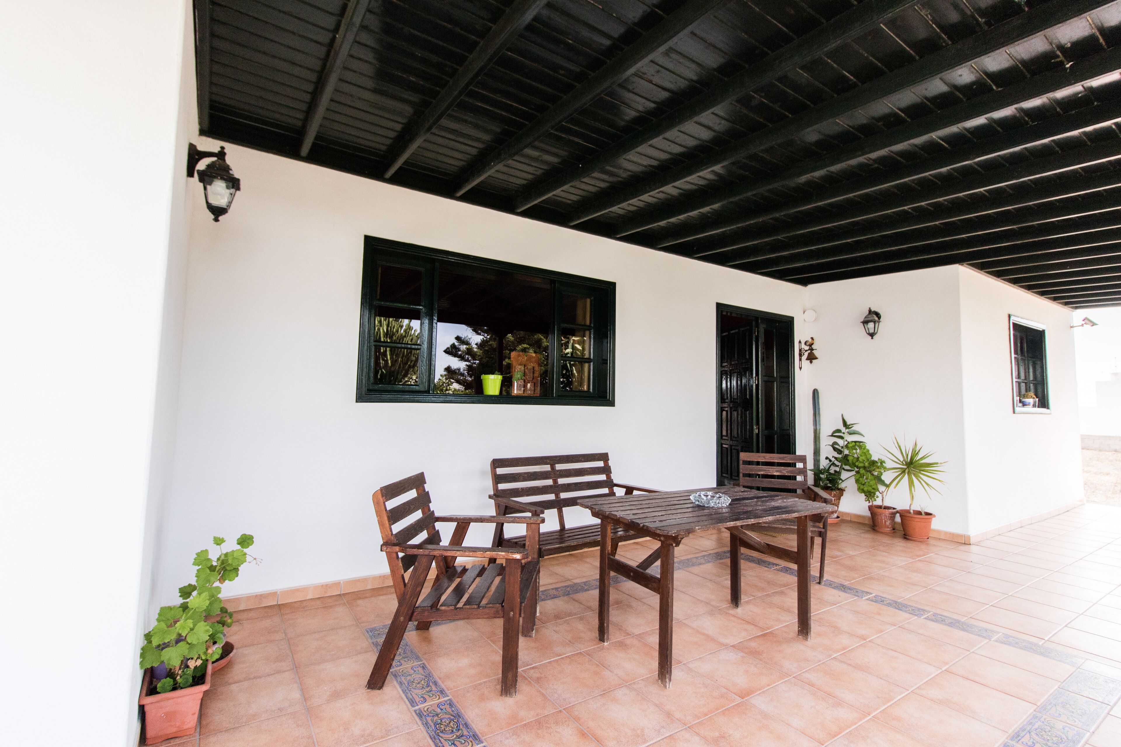 Un patio al aire libre con mesa y sillas de madera, rodeado de plantas en macetas.