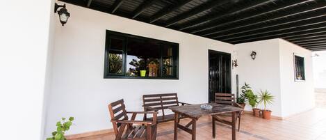 Un patio al aire libre con mesa y sillas de madera, rodeado de plantas en macetas.