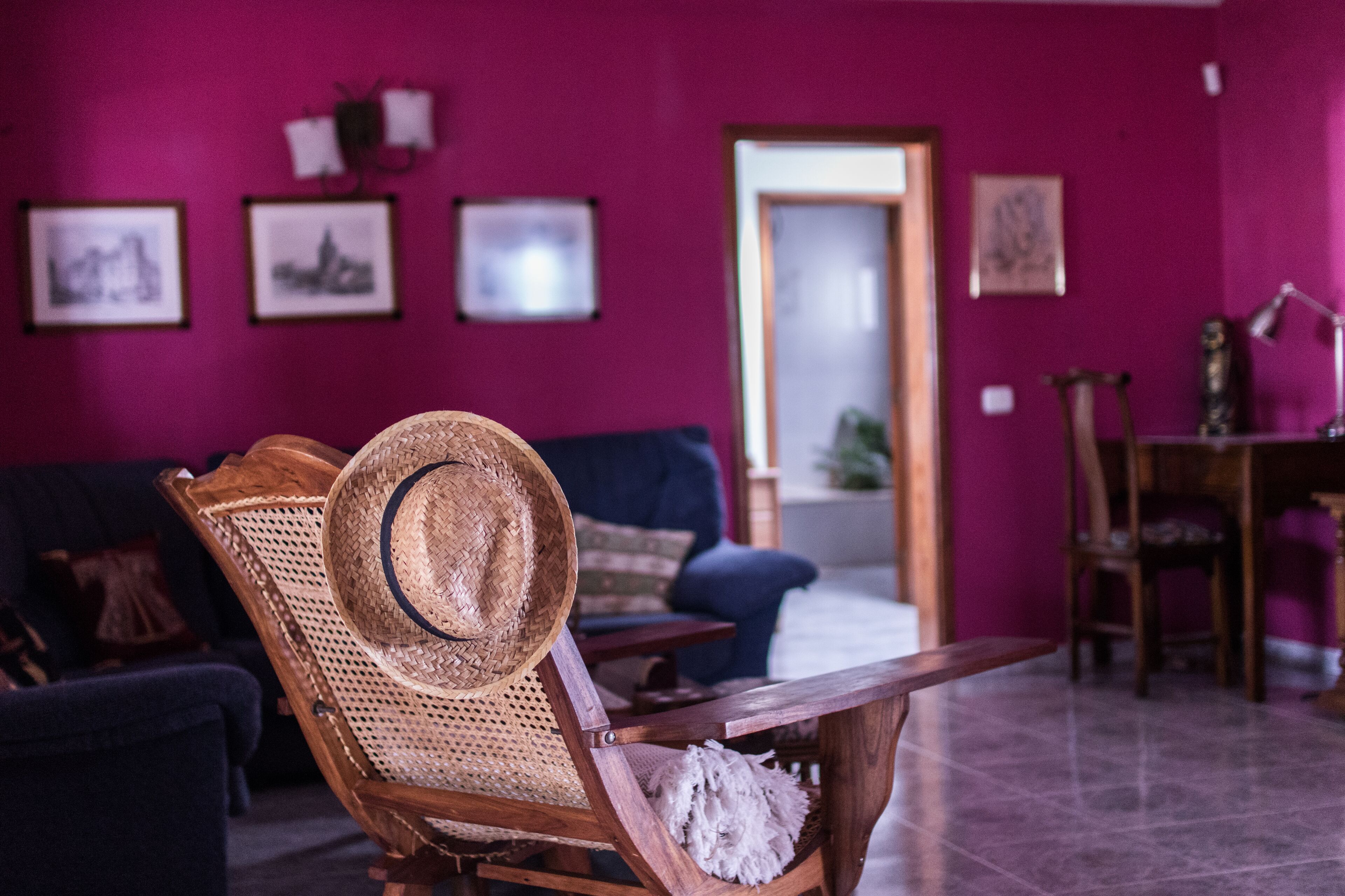 Une pièce comprenant une chaise en bois avec un siège en osier, un chapeau, un canapé bleu foncé et une table en bois.