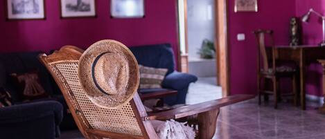 Une pièce comprenant une chaise en bois avec un siège en osier, un chapeau, un canapé bleu foncé et une table en bois.