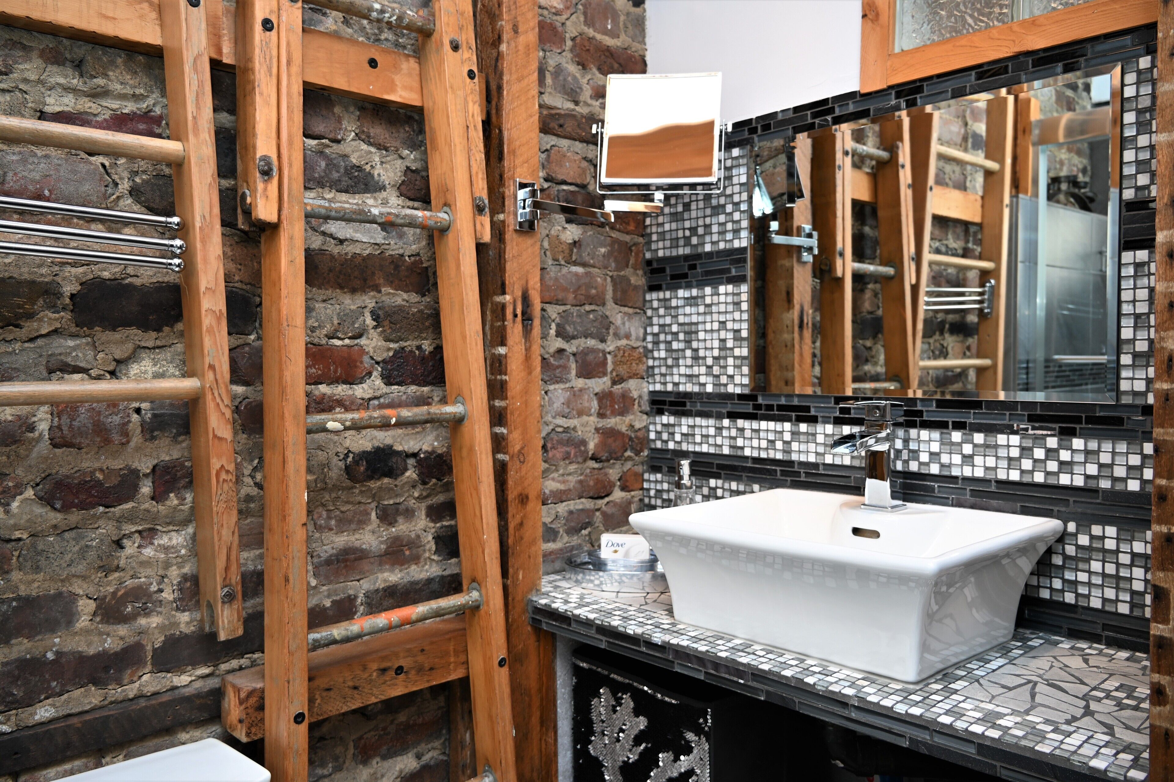 A bathroom with a white sink, a wooden ladder, and a tiled backsplash.