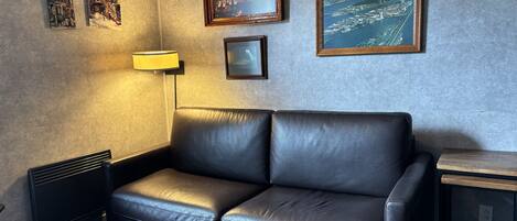 A modern living room with a black leather sofa, a standing lamp, and framed artwork on the wall.