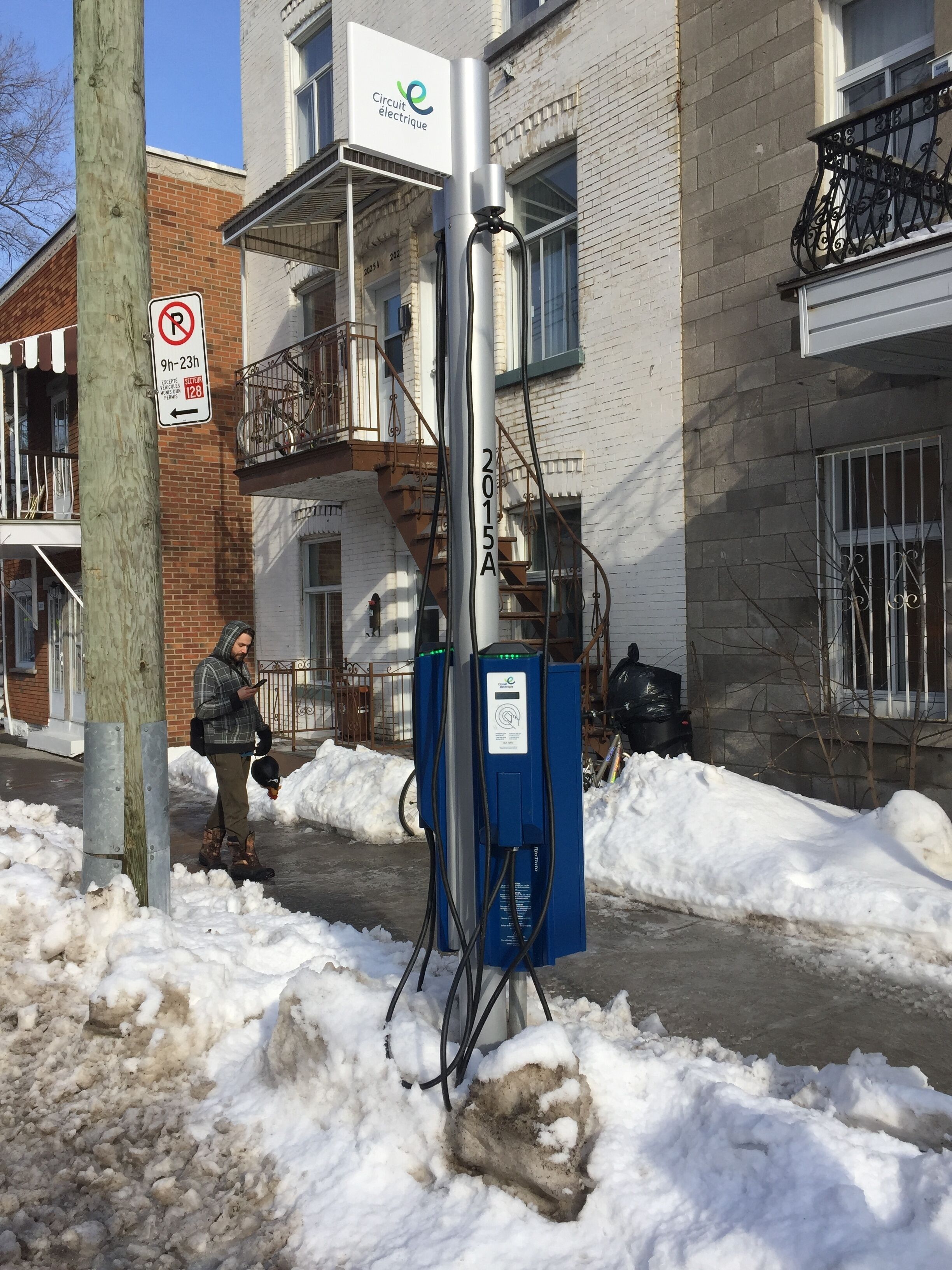 Un poste de electricidad con una acera nevada y un cartel de no estacionamiento.