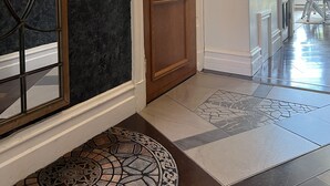 A hallway with a wooden door, a glass panel door, and a patterned rug leading to a dining area.