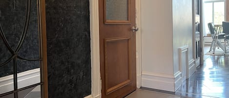 En hall med en dörr av trä, en dörr med glaspanel och en mönstrad matta som leder till en matplats.