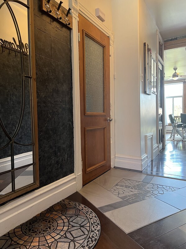 A hallway with a wooden door, a glass panel door, and a patterned rug leading to a dining area.