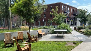 A park with wooden chairs and a picnic table, surrounded by grass and trees.