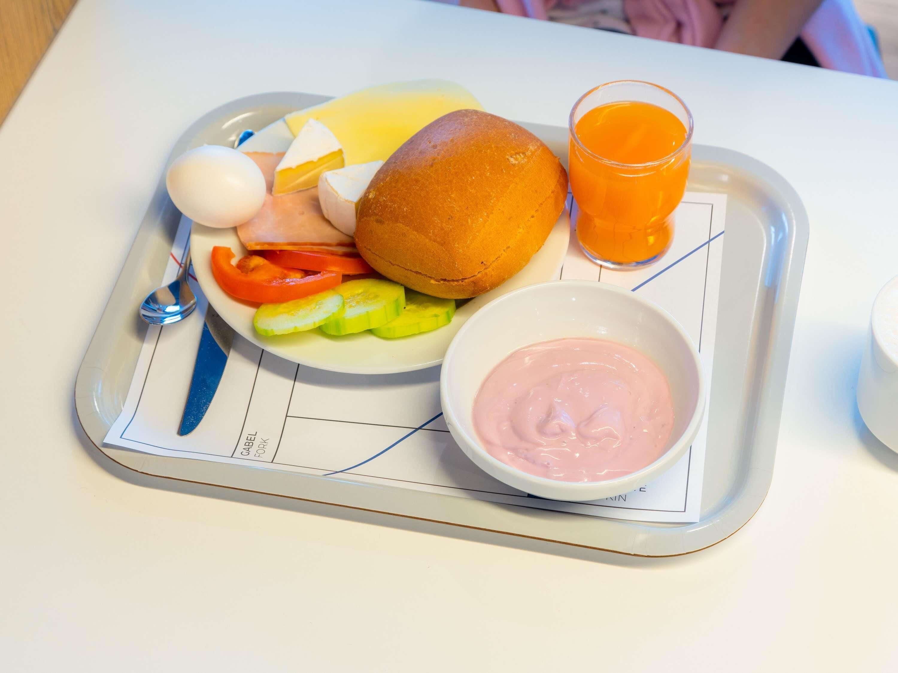 A tray with a sandwich, egg, vegetables, a glass of orange juice, and a bowl of pink sauce.