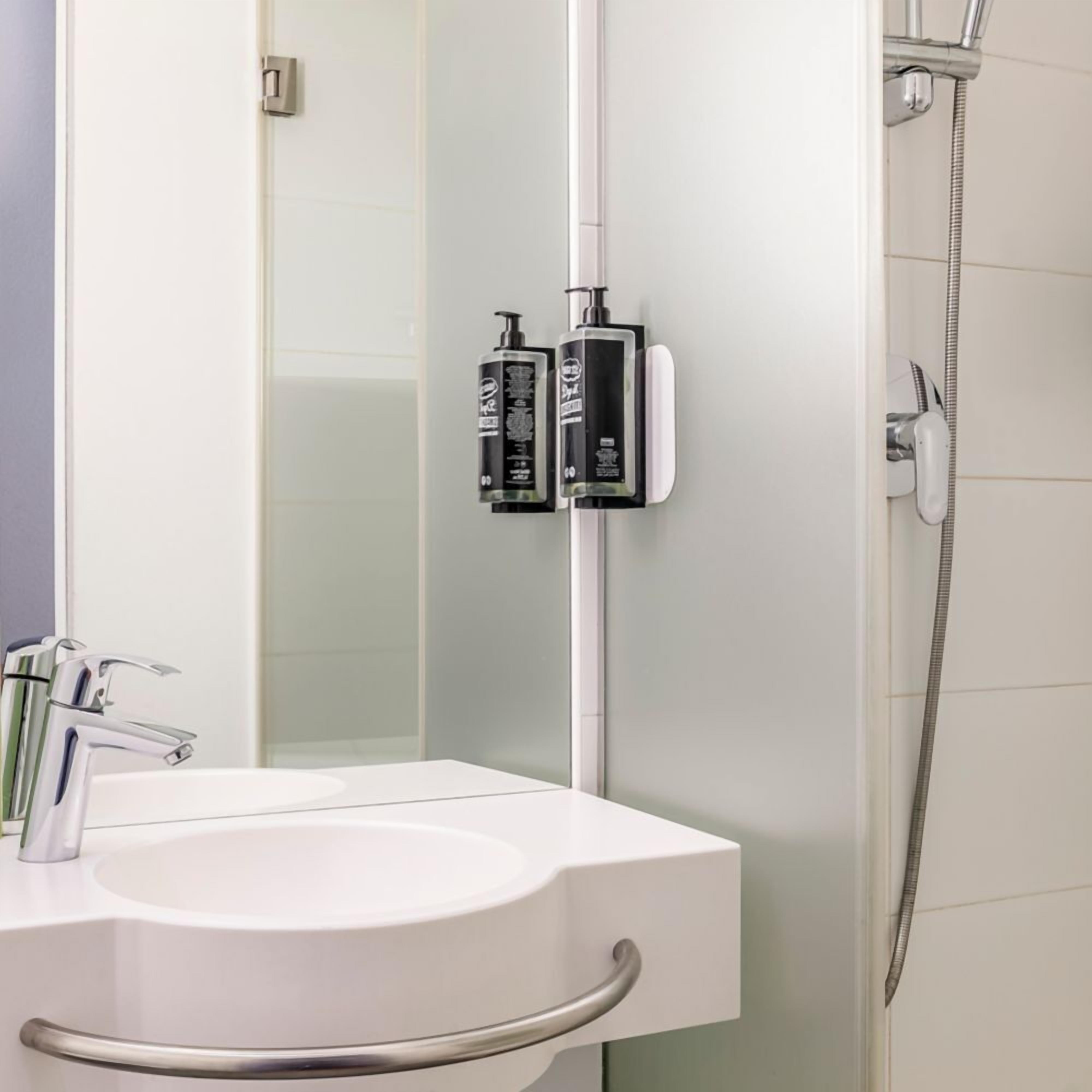 Un baño con lavamanos blanco, espejo y ducha.