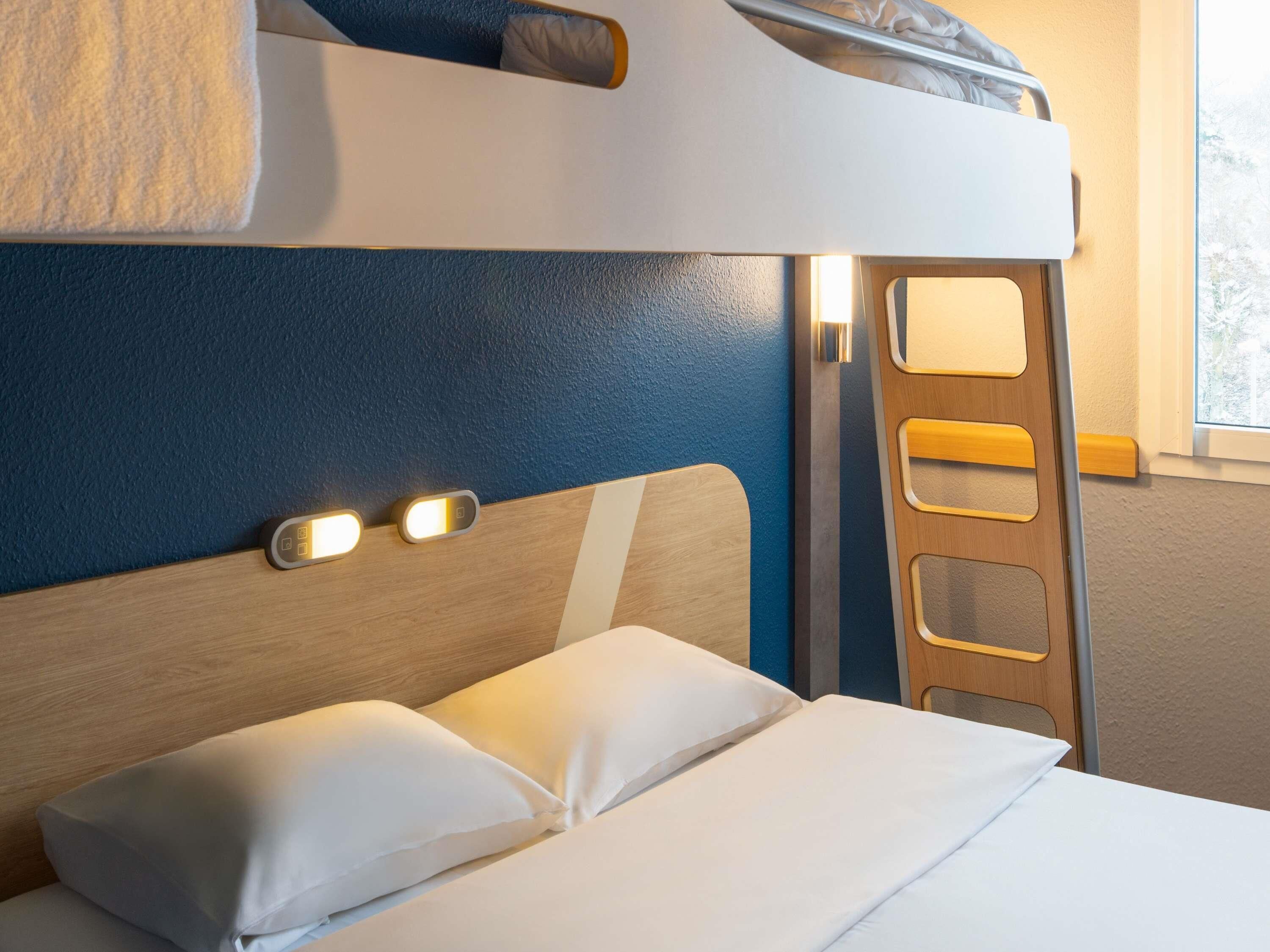 Un lit superposé avec une tête de lit, deux oreillers et une table de chevet avec une lampe.