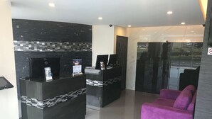 Un espace d’accueil avec un comptoir noir, un écran numérique et un canapé violet.