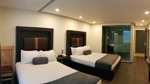 Une chambre d’hôtel avec deux lits, une chaise en bois, une petite table avec un téléphone et une porte en verre donnant sur une salle de bain.