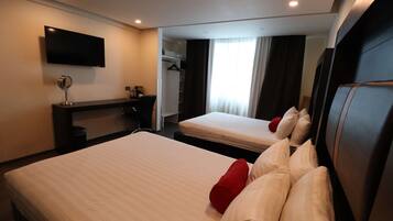 A hotel room with two beds, a TV mounted on the wall, a desk with a mirror, and a wardrobe.