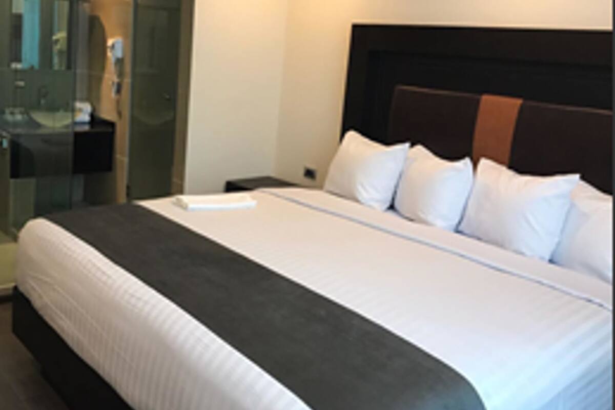 A hotel room with a large bed, a bedside table, a glass shower enclosure, and a dark headboard.