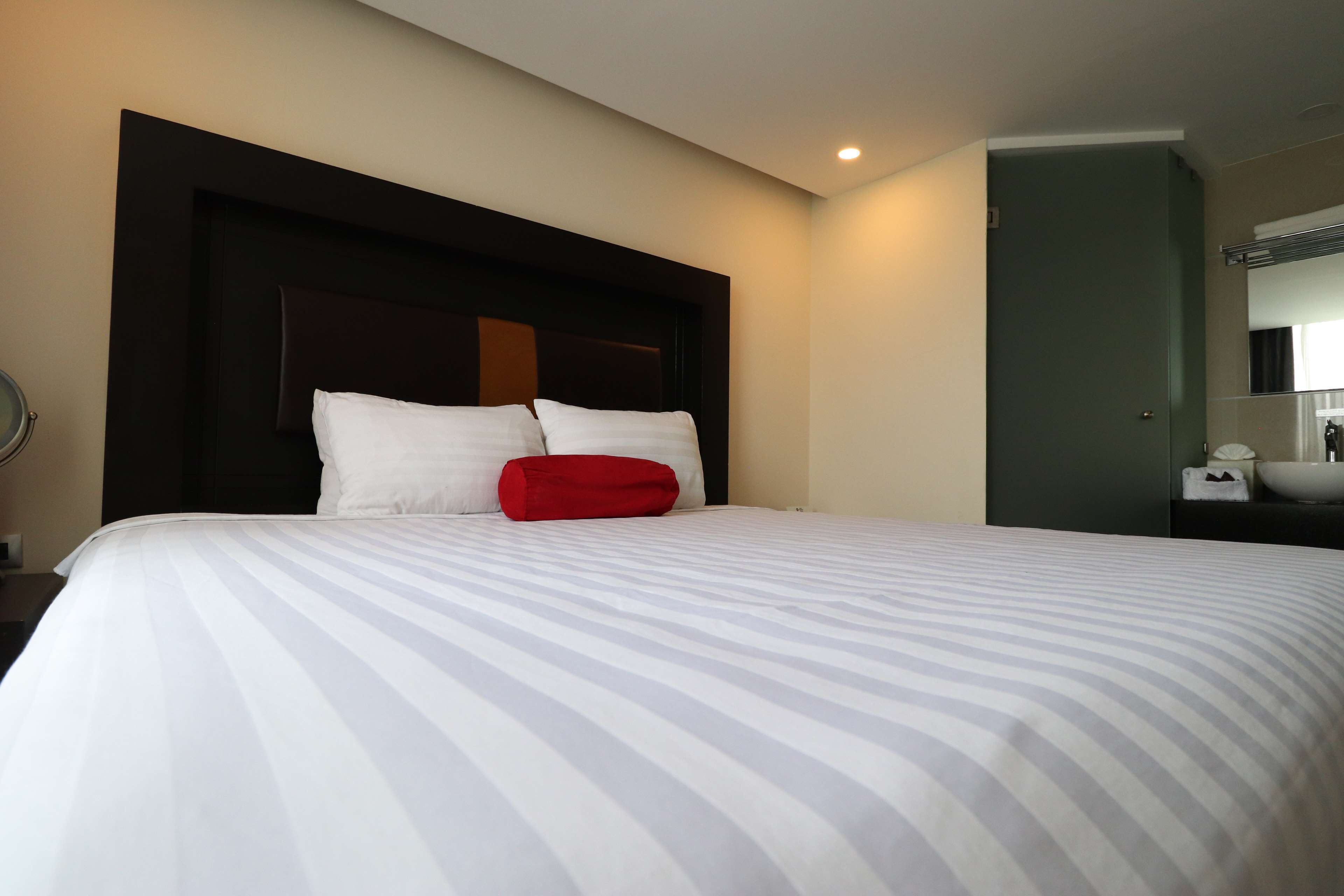 Una habitación de hotel con una cama grande, un cabecero oscuro y un baño con lavamanos y espejo.