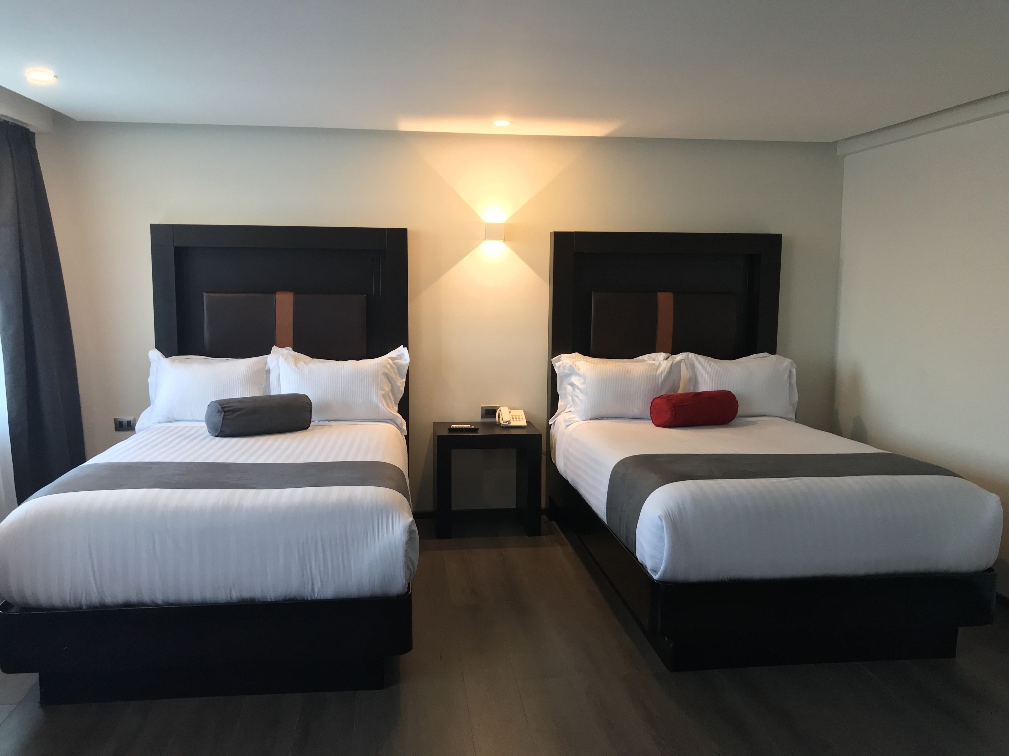 A hotel room with two beds, each with a headboard, a bedside table, and a lamp.