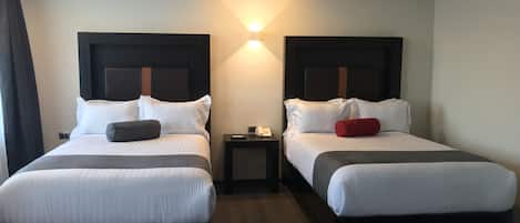 A hotel room with two beds, each with a headboard, a bedside table, and a lamp.