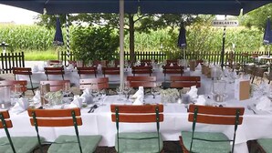 An outdoor dining area with tables set for a meal, surrounded by wooden benches and covered by a blue canopy. - Landgasthof Alt-Enginger Mühle (Paderborn)