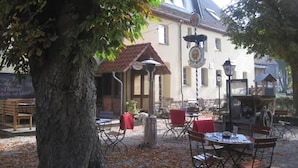 An outdoor seating area with tables and chairs, a tree, and a building with a tiled roof in the background. - Landgasthof Alt-Enginger Mühle (Paderborn)