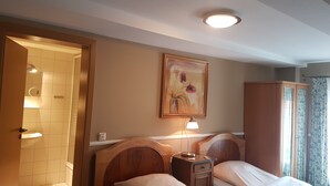 A hotel room with two beds, a wooden headboard, a bedside table with a lamp, a painting on the wall, and a window with curtains. - Landgasthof Alt-Enginger Mühle (Paderborn)