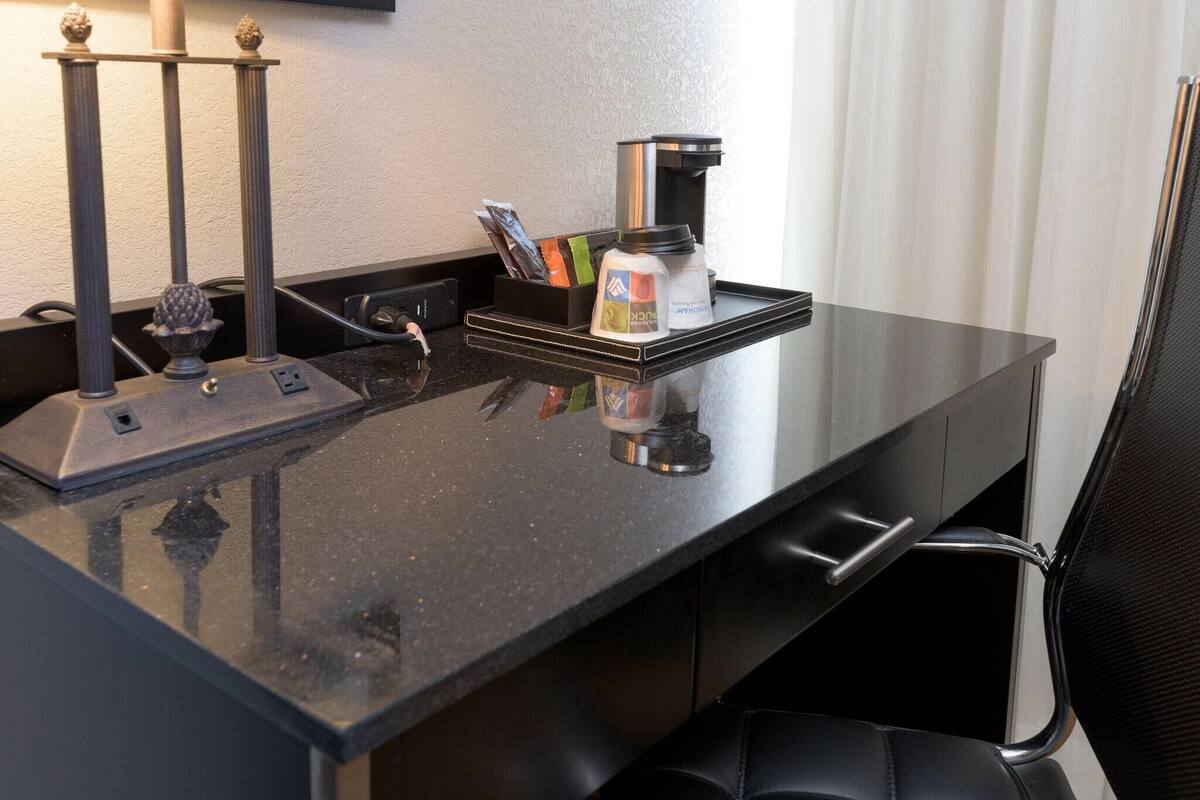 Mostrador de hotel con cafetera, botella de agua y bandeja con varios objetos.