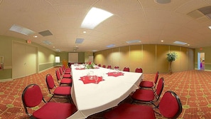 Un salón de conferencias con una larga mesa, sillas rojas y piso alfombrado.