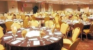 Un salón de banquetes con mesas redondas dispuestas para cenar, cada una con su vajilla y centros de mesa.