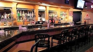 A bar area with a counter, multiple chairs, and a television screen mounted on the wall. - Ramada by Wyndham Boise (Boise)