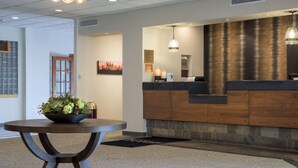 A reception area with a wooden reception desk, a black and white patterned rug, and a plant on a round table. - Ramada by Wyndham Boise (Boise)
