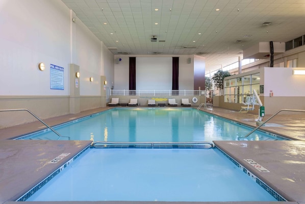 Una piscina interior amb aigua cristal·lina, un cartell de normes de la zona de la piscina i una barana blanca.