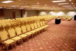 Una sala de conferències amb files de cadires grogues, un sòl amb moqueta i una zona d'escenari.