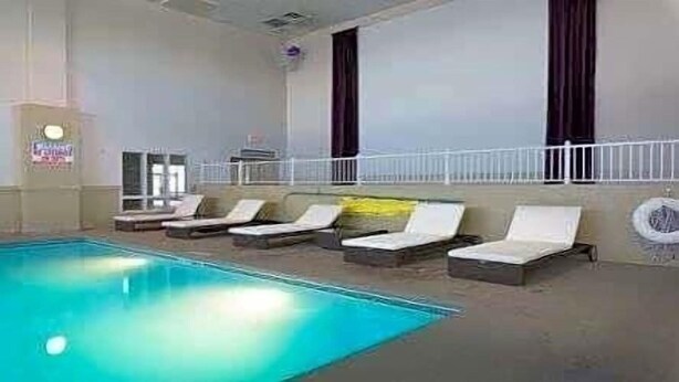 An indoor swimming pool with lounge chairs and a white railing. - Ramada by Wyndham Boise (Boise)