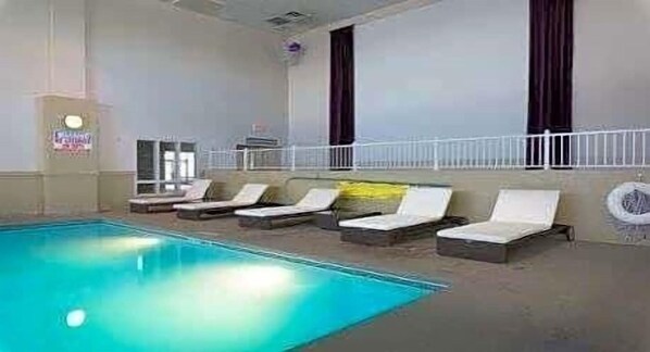 Una piscina interior con sillas de descanso y barandilla blanca.