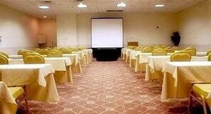 A conference room with rows of tables and chairs, a projector screen, and a carpeted floor. - Ramada by Wyndham Boise (Boise)
