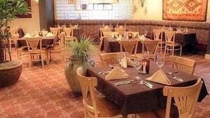 A restaurant with wooden tables and chairs, potted plants, and a patterned carpet. - Ramada by Wyndham Boise (Boise)