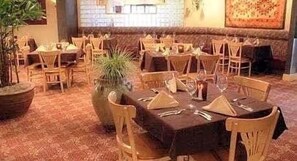 Un restaurante con mesas y sillas de madera, plantas en macetas y una alfombra estampada.