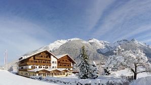 Un immeuble en bois à plusieurs étages, doté de balcons, entouré d’arbres et de montagnes couverts de neige.