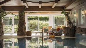 Une piscine intérieure agrémentée de piliers en pierre, de meubles en osier et offrant une vue sur le jardin.