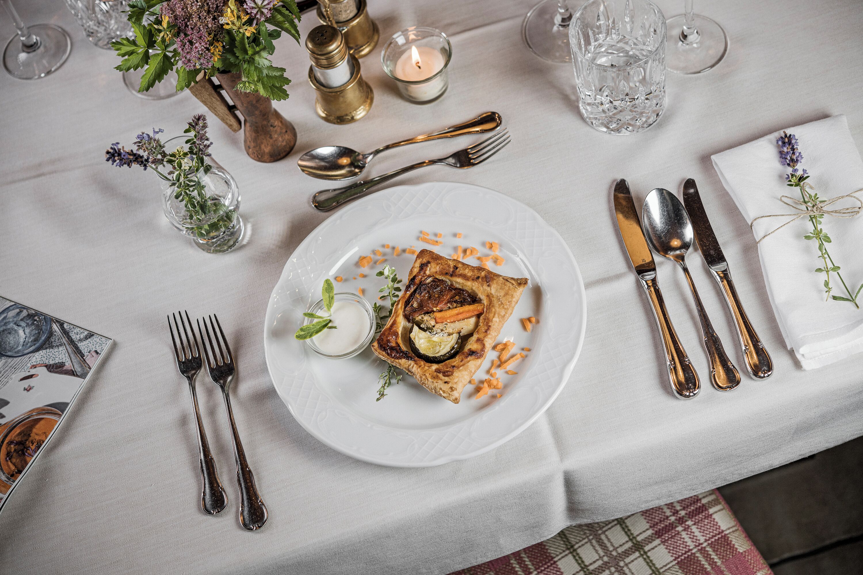 Una mesa dispuesta con un plato blanco, cubiertos y una vela.