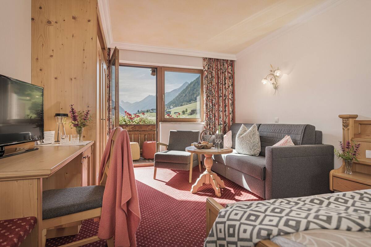 Um quarto aconchegante com televisão, sofá, cama, escrivaninha e janela com vista para as montanhas.