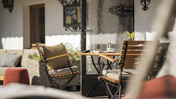 Un área de estar acogedora al aire libre con sillones de mimbre y una mesa de madera, un sofá con cojines y una pared decorativa con un espejo y obras de arte.