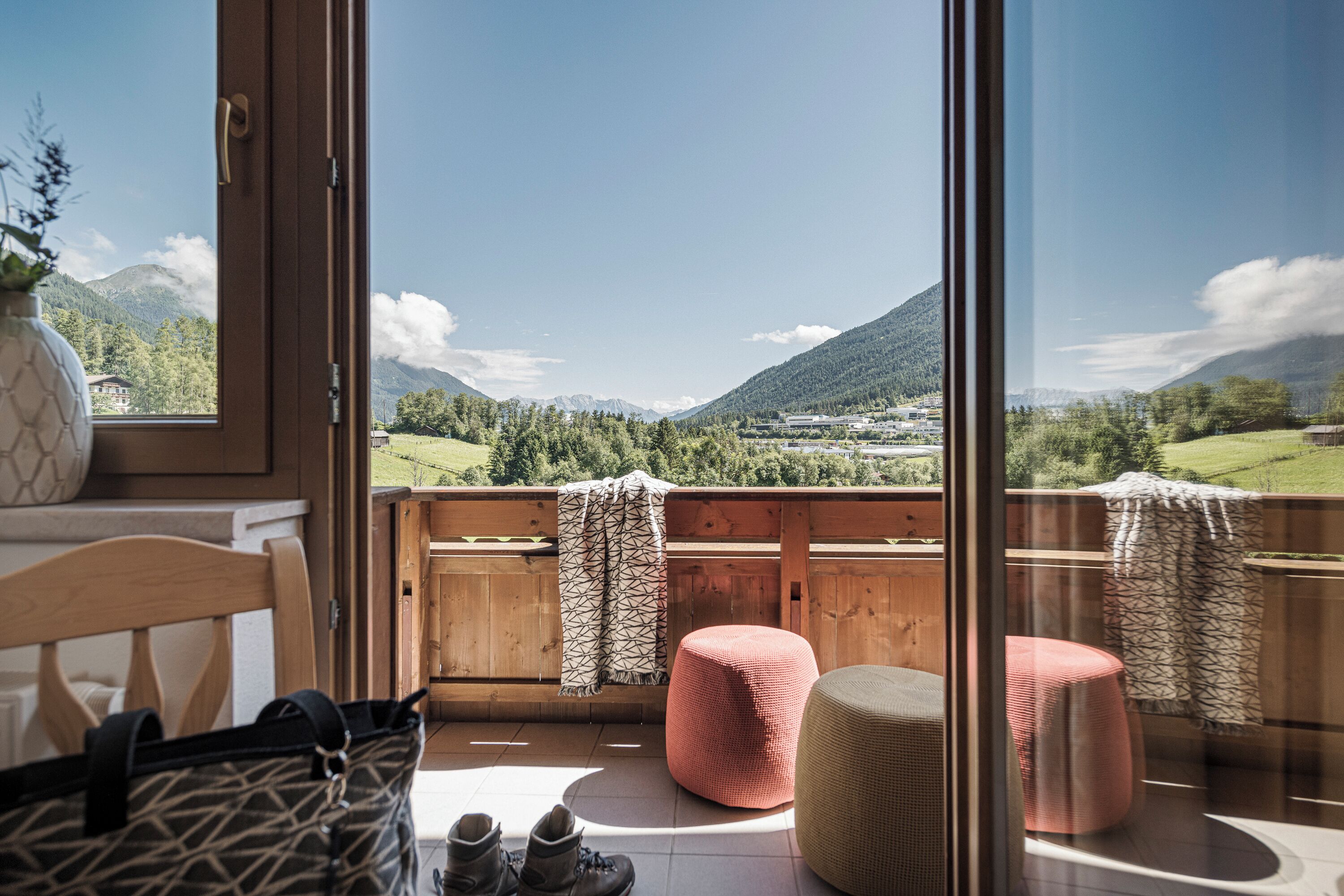 A balcony with a wooden railing, a wicker ottoman, and a pair of boots.